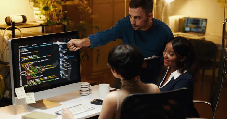 Man presenting to colleague in office meeting, pointing at screen during discussion.