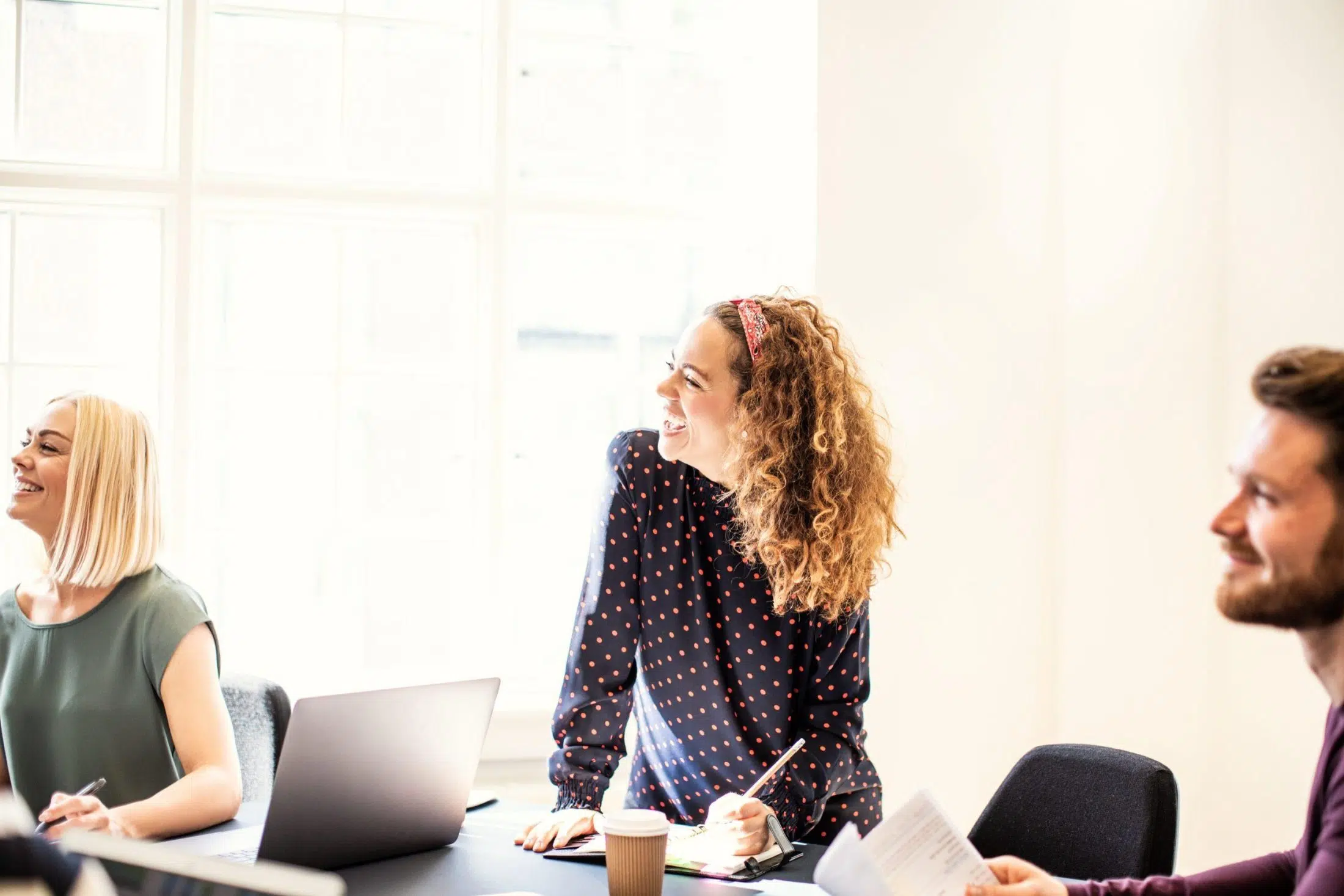 Laughing young businesswoman working with a group of colleagues sitting around a boardroom table in an office