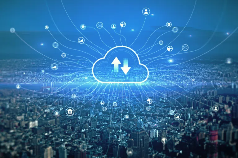 The image presents a wide, aerial view of a densely built modern cityscape stretching across the entire lower half of the frame, captured under a cool blue color tone that gives the scene a sleek, technological atmosphere, while dominating the center of the composition is a large, glowing cloud icon positioned above the city, outlined in bright cyan light; inside the cloud symbol are two bold arrows—one pointing upward and one downward—clearly representing data upload and download processes, and radiating outward from this central cloud are numerous thin, luminous lines that extend in all directions across the sky and down into the city, visually connecting to multiple small circular icons scattered throughout the scene, each icon representing different digital functions or services such as user accounts, devices, communication tools, and applications; these interconnected lines create a web-like network overlay that integrates seamlessly with the buildings