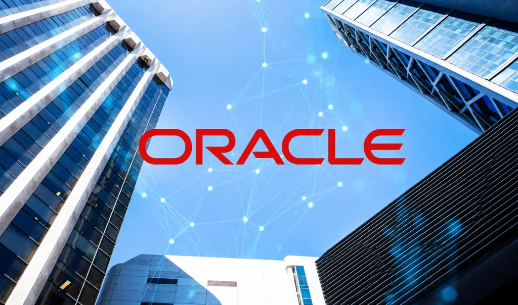 Oracle logo displayed against a background of modern high-rise office buildings viewed from below, with blue digital network lines and glowing connection points across the sky, symbolizing cloud technology, data connectivity, and enterprise digital infrastructure.
