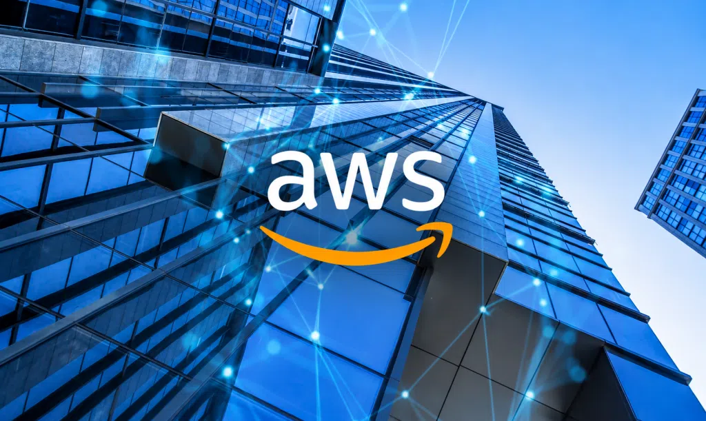 AWS logo displayed over a low-angle view of modern glass skyscrapers, with blue digital network connections and glowing nodes overlaid to represent cloud computing, connectivity, and enterprise technology infrastructure.