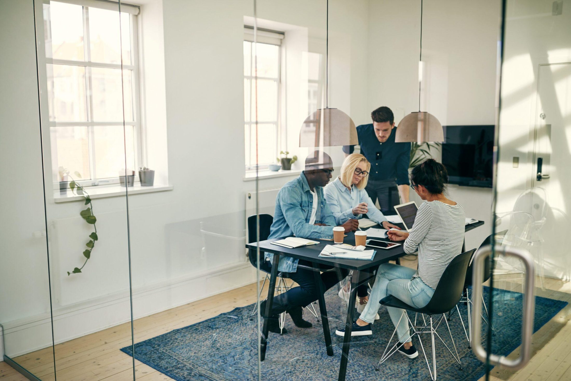 Four people around a desk looking at documents and laptops discussing Human Capital Management (HCM) Consulting Services