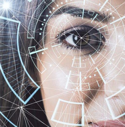 The image presents a close-up of part of a human face, focusing on one eye, overlaid with futuristic digital interface graphics. The eye is sharply in focus, while the rest of the face is partially cropped and softly blurred, drawing attention to the iris and surrounding area. Across the image, translucent geometric lines and nodes form a network-like pattern, suggesting data connections or artificial intelligence systems. Circular interface elements and targeting-style graphics are layered around the eye, resembling biometric scanning or facial recognition technology. The background transitions into a gradient of dark blue and grey tones, reinforcing a high-tech atmosphere. The combination of the human feature and digital overlays creates a visual theme centered on advanced technology, data analysis, and biometric identification systems.