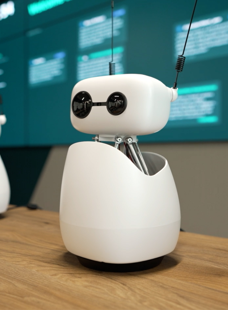 A small, white, friendly-looking AI robot with rounded edges and antennae sits on a wooden table, featuring two black circular eyes and an open-body design that reveals internal components, with blurred digital screens in the background suggesting a modern tech environment.
