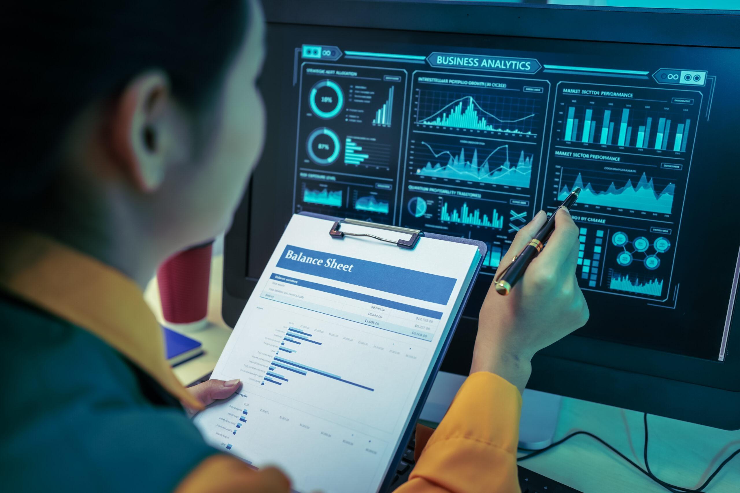 An Asian businesswoman analyzes digital charts on a computer screen, reviewing performance reports