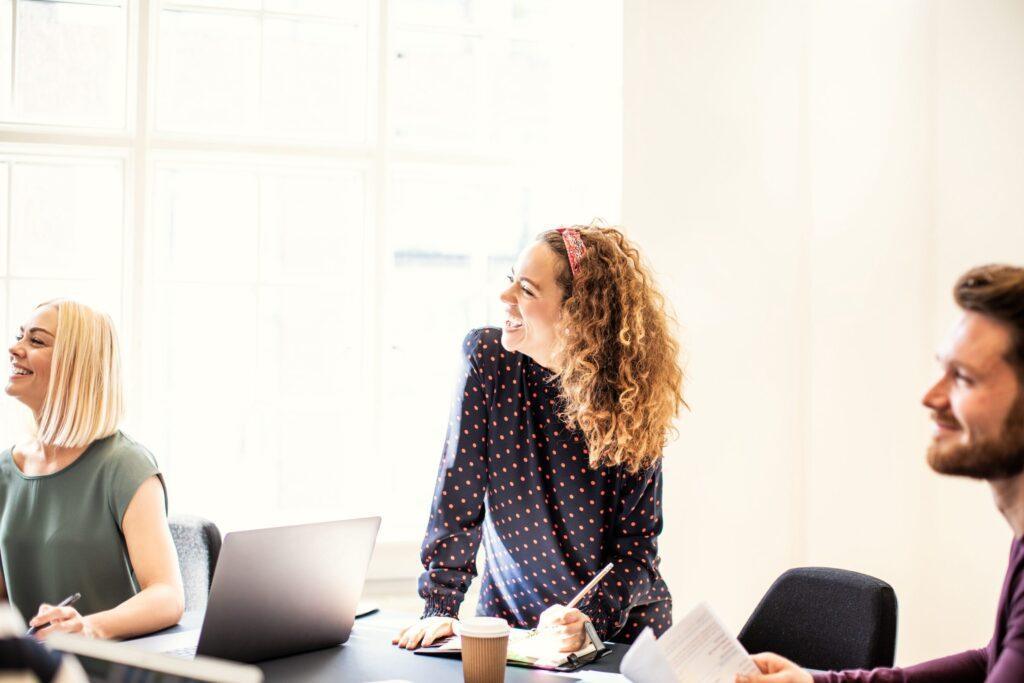 Laughing young businesswoman working with a group of colleagues sitting around a boardroom table in an office
