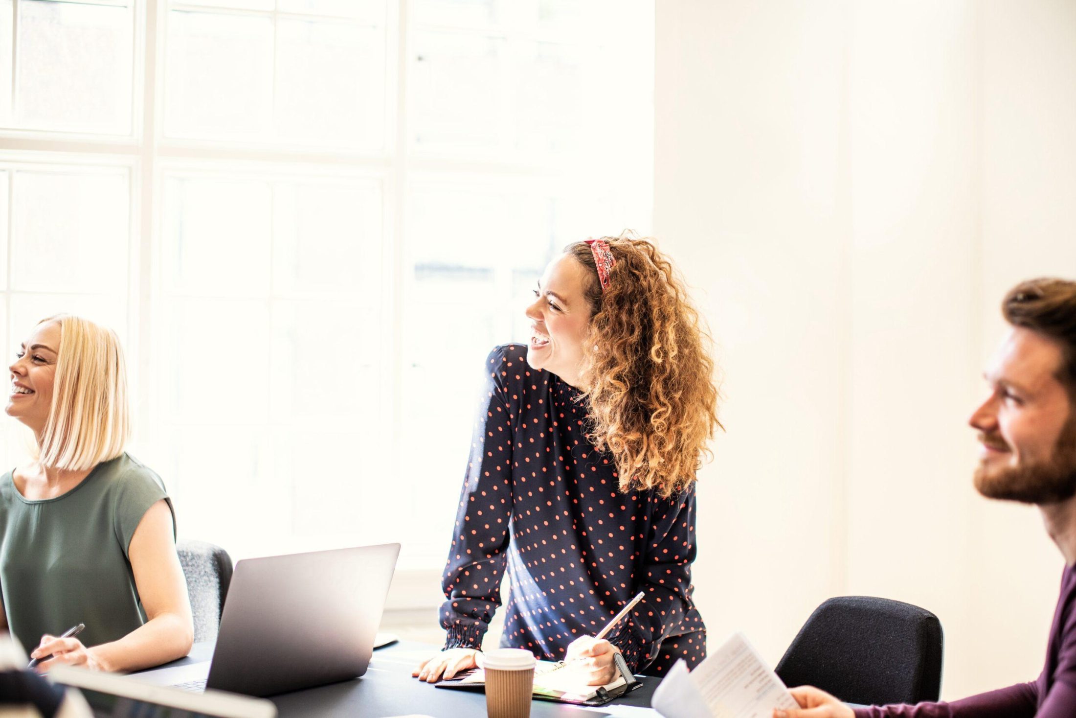 Laughing young businesswoman working with a group of colleagues sitting around a boardroom table in an office
