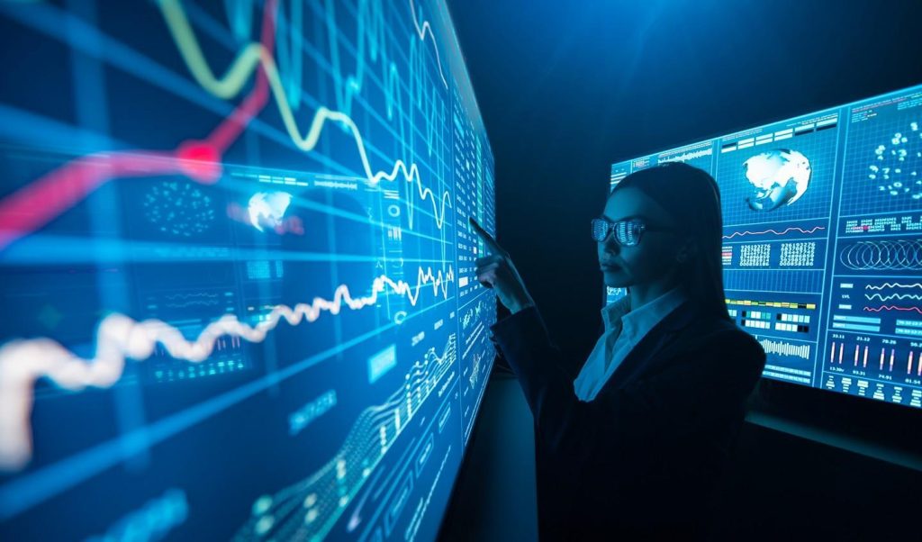 A person stands in a dark, high‑tech room, pointing at large blue digital dashboards filled with line charts, graphs, and world‑map data displayed across multiple wall‑sized screens.