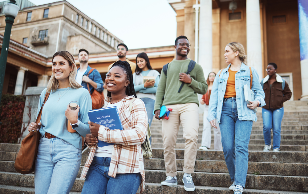 Diverse group of university students walking down campus steps, smiling and carrying books and backpacks.