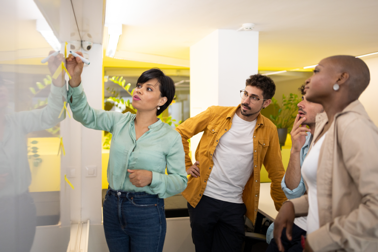 Team collaborating in a modern office, reviewing ideas on a glass whiteboard during a business transformation workshop.