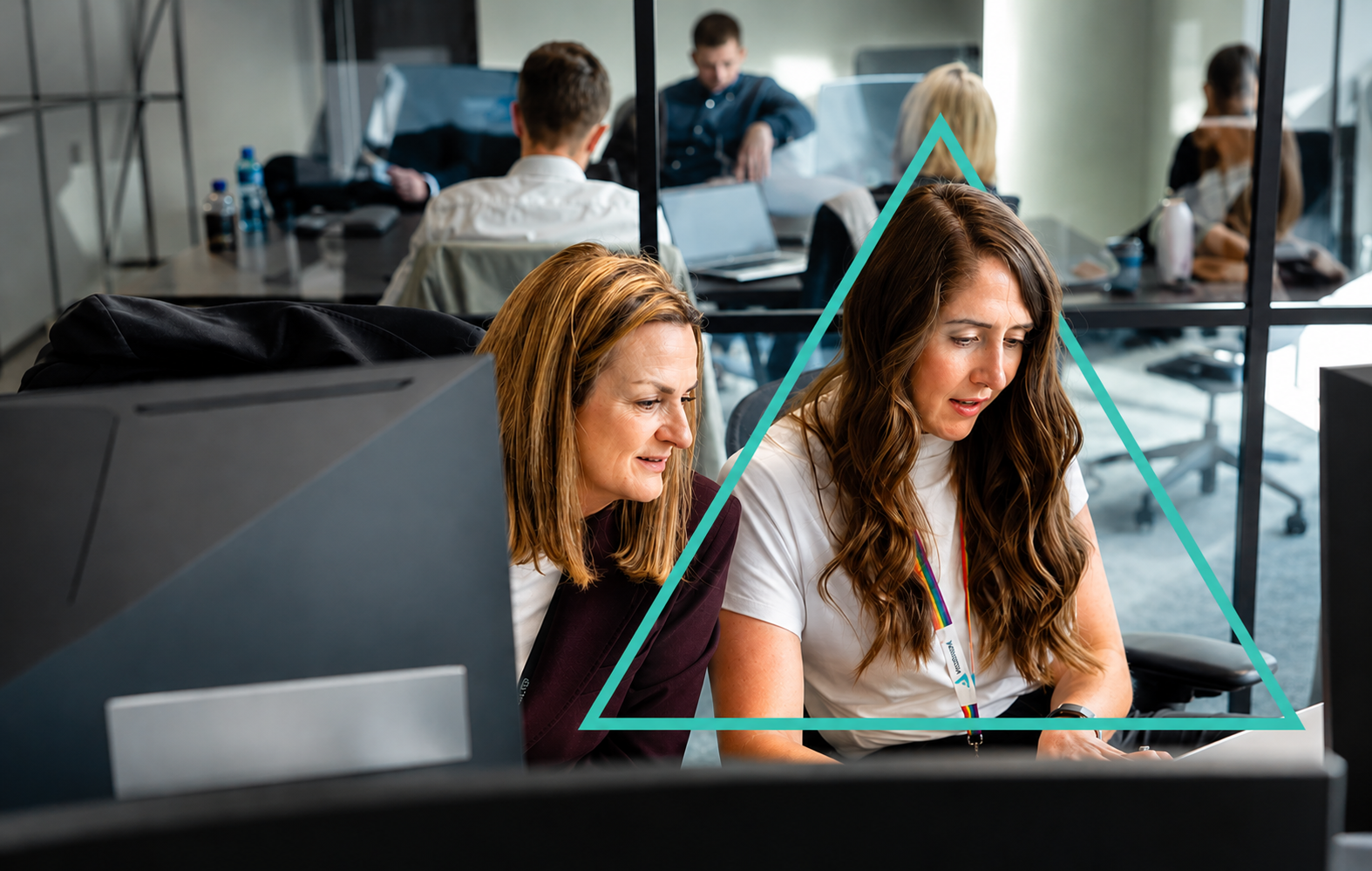 Two colleagues collaborating at a computer in a modern office, with a teal triangular graphic overlay framing them.